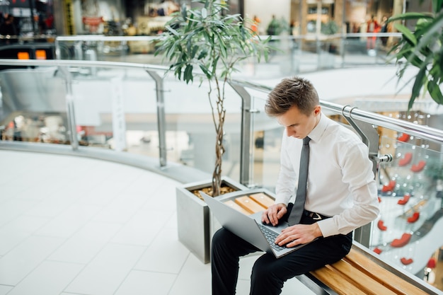 Ordinateur portable de travail étudiant, vêtu d'une chemise blanche, jeune étudiant utilisant un ordinateur portable, dans un centre commercial, s'assit, à l'intérieur, centre d'affaires, s'assit