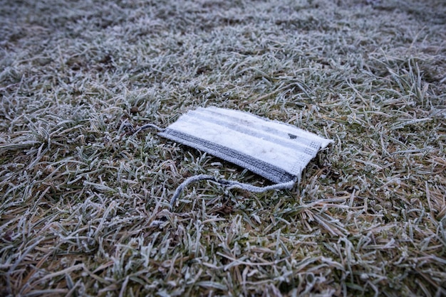 Ordures de masque facial sur l'herbe givrée au sol en hiver