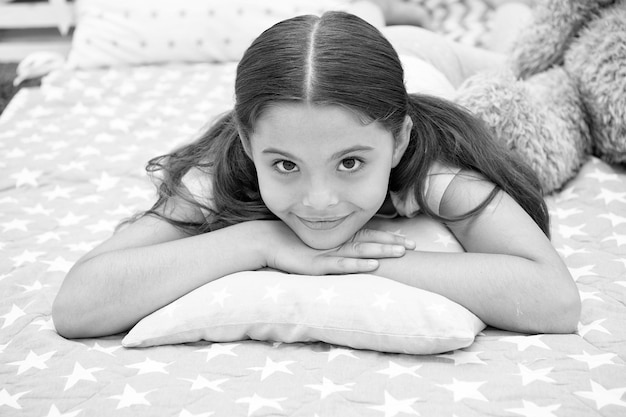 Oreiller confortable Fille souriante enfant heureuse allongée sur le lit avec des oreillers à motif d'étoiles et un plaid mignon dans sa chambre Literie pour enfants Fille enfant se réveillant le matin Literie à la mode moderne