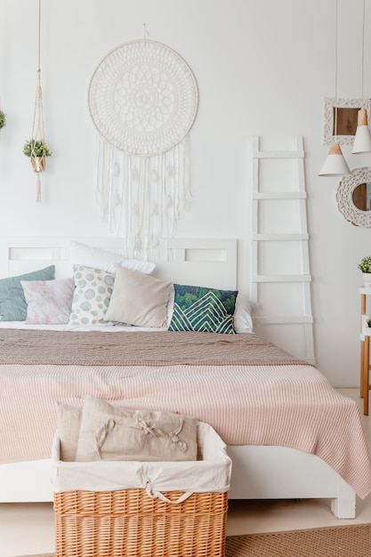 Oreiller vert et beige sur le lit dans la chambre avec des draps de couleur pastel sur le lit. design élégant de l'appartement dans le style lagom.Intérieur blanc scandinave élégant avec lit, plante tropicale, couverture confortable.