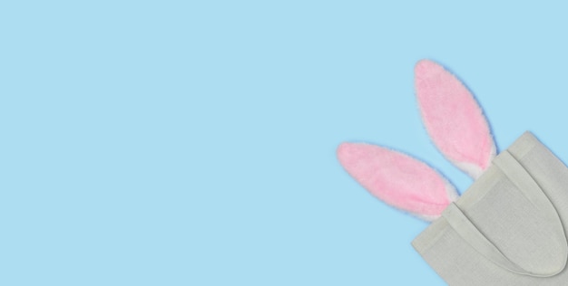 Oreilles de lapin de Pâques rose bannière sortant du sac textile réutilisable sur un bleu