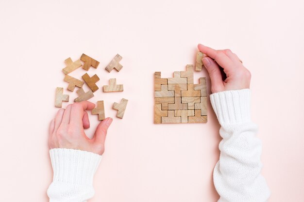 Organisation et ordre. Des mains féminines étalent des pièces de puzzle en bois sur fond rose.