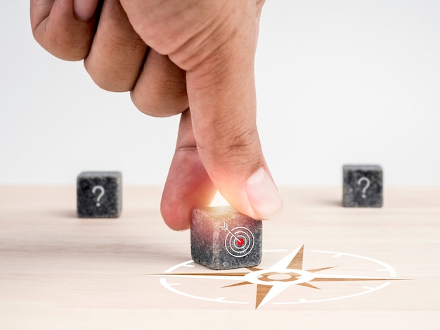 Orientations des objectifs commerciaux, solution commerciale, concept de public cible. Mettez à la main les blocs de cube noir avec le symbole de l'icône cible avec le signe de la boussole sur une table en bois sur fond blanc, style minimal.