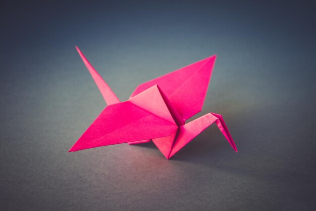 Origami grue en papier rose isolé sur fond gris