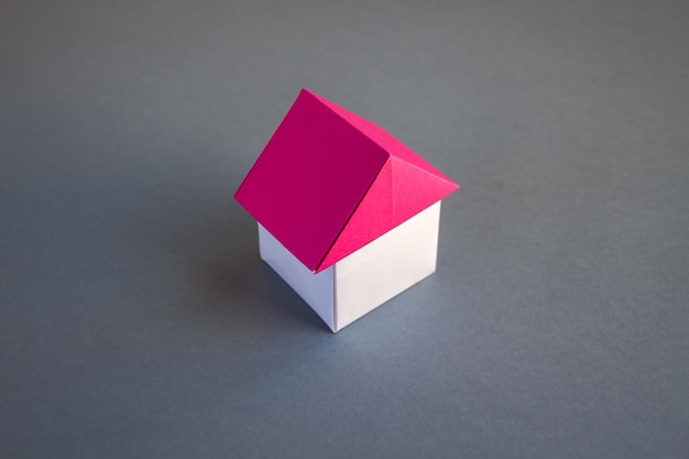 Origami de maison de papier blanc et rouge isolé sur fond gris