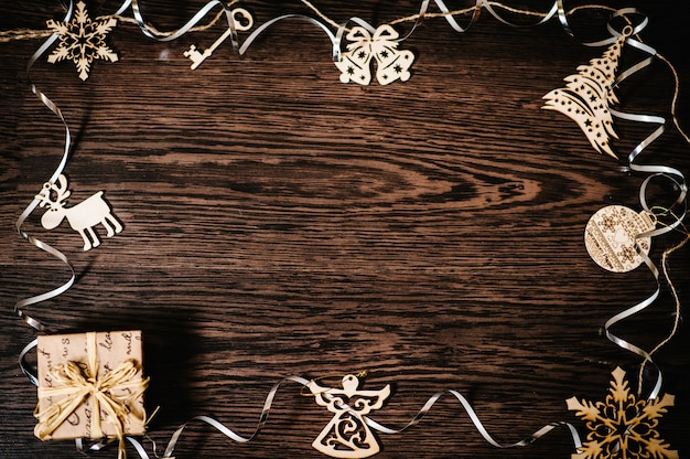 Ornements d'arbre de Noël, cadeau, boîte avec rubans, flocons de neige, cloches, cerf, ange sur fond de bois structurel brun. pose à plat. vue de dessus, cadre avec espace pour le texte. joyeuses fêtes.