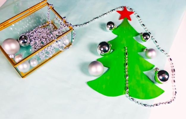Des ornements en argent sortent d'un cercueil en verre et en or et décorent un sapin de Noël plat sur fond noir et bleu