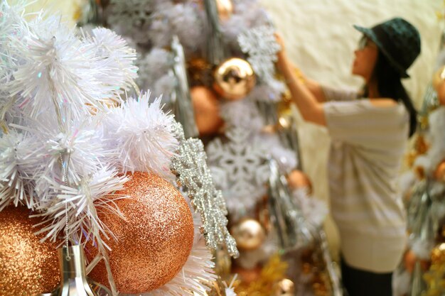 Ornements de Noël or scintillant avec femme floue décorant l'arbre de Noël en arrière-plan