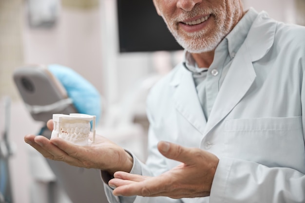 un orthodontiste âgé expérimenté tenant un moule en plâtre dentaire dans sa main