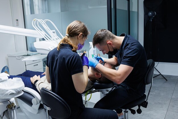 Un orthodontiste avec un assistant traite les dents à l'aide d'instruments dentaires Cabinet dentaire Traitement orthodontique des dents