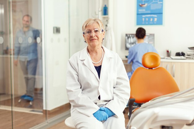 Photo orthodontiste senior en uniforme médical assis sur une chaise regardant vers l'avant en attente d'un homme patient pour commencer un traitement de stomatologie après une chirurgie dentaire