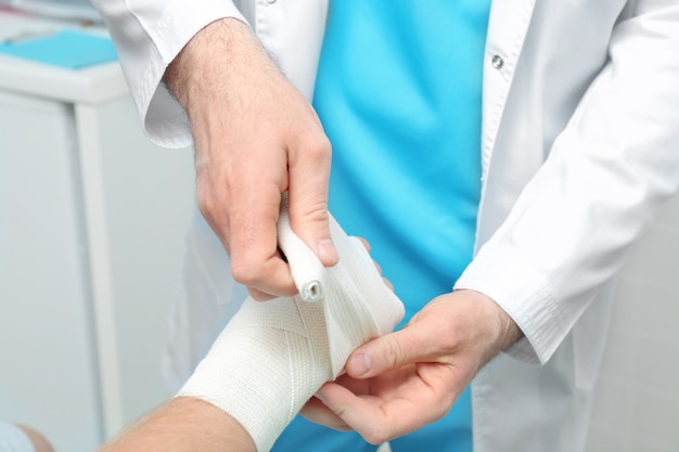 Orthopédiste appliquant un bandage sur la main du patient en clinique, gros plan