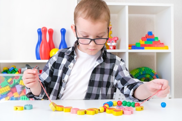 Orthophonie, développement de la motricité fine. Un petit garçon enfile des perles sur une ficelle. enfant heureux