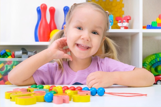 Orthophonie, développement de la motricité fine. La petite fille enfile des perles sur une ficelle.