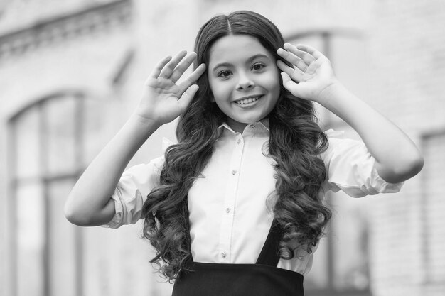 Osez être belle Un enfant heureux fixe une longue coiffure bouclée à l'extérieur Look de retour à l'école Mode scolaire Look de beauté Salon de coiffure Éducation élémentaire Journée de la connaissance 1er septembre