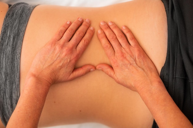 Photo osteopathie physiothérapie crânienne sur le dos d'une femme pour éviter les maux de dos