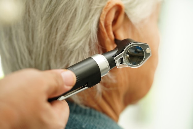 Photo otolaryngologiste ou médecin orl examinant l'oreille d'un patient âgé présentant un problème de perte auditive à l'otoscope