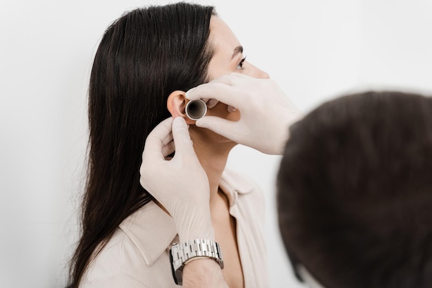 Otoscopie L'oto-rhino-laryngologiste regarde à travers l'otoscope les oreilles de la femme Traitement de la douleur à l'oreille Médecin ORL avec entonnoir auriculaire