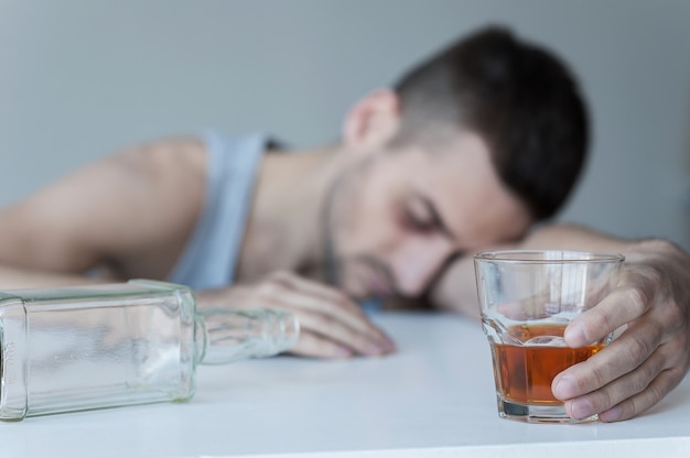 Oublier ses problèmes. Jeune homme assis à la table avec une bouteille vide dessus et gardant les yeux fermés