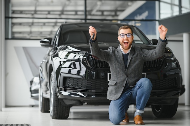 Oui, c'est ma nouvelle voiture Client chez un concessionnaire automobile Jeune homme s'agenouilla avec les clés en main