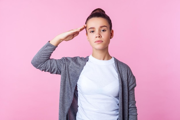 Oui monsieur Portrait d'une adolescente brune obéissante avec une coiffure chignon dans des vêtements décontractés saluant l'écoute de l'ordre avec une expression responsable sérieuse prise en studio isolée sur fond rose