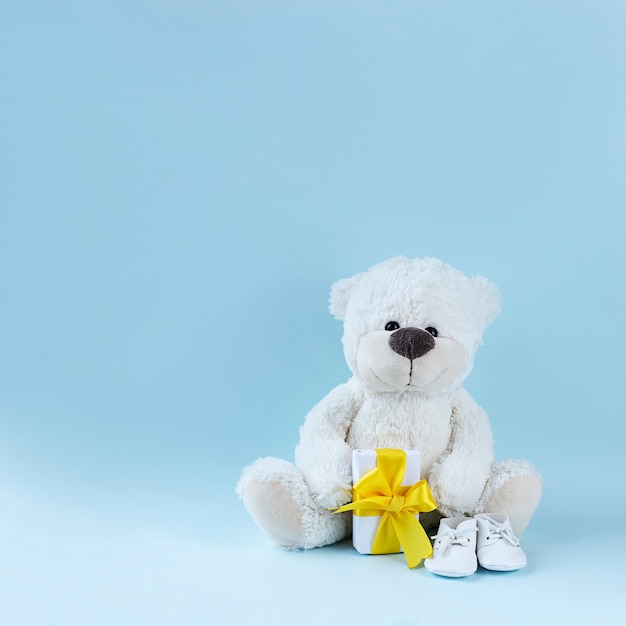 Ours en peluche blanc, chaussons pour bébé et petit cadeau avec ruban jaune sur une surface bleu clair