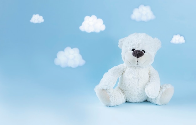 Photo ours en peluche blanc et petits nuages autour sur une surface bleu clair