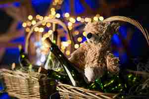 Photo ours en peluche bouteille de champagne avec panier de noël guirlandes d'or sur fond de bois brun foncé célébration du nouvel an conceptxa