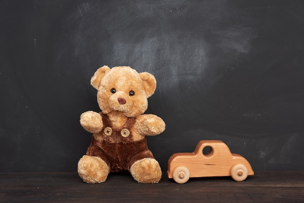 Ours en peluche brun est assis sur une table en bois marron et une voiture en bois