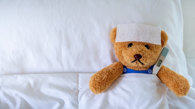 L'ours en peluche dormait avec une forte fièvre dans le lit. Avec un thermomètre.