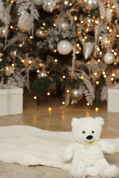 Un ours en peluche est assis près d'un sapin de Noël rougeoyant décoré