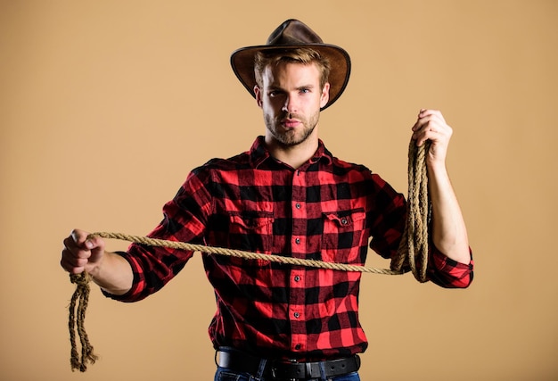 Outil de lasso de cow-boy américain Occupations de ranch Le lasso est utilisé dans les rodéos en partie les événements compétitifs Le lasso peut être attaché ou enveloppé La vie occidentale Homme cow-boy fond beige Homme portant un chapeau tenir la corde