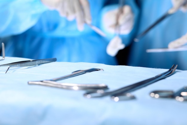 Outils chirurgicaux allongés sur la table tandis qu'un groupe de chirurgiens à l'arrière-plan patient opérant des instruments médicaux en acier prêts à être utilisés