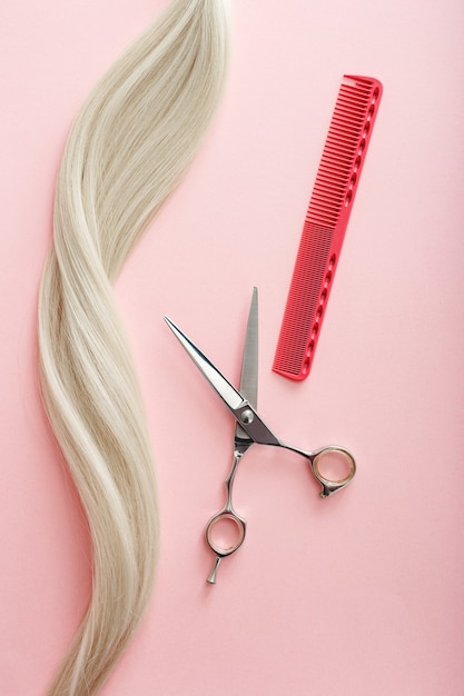 Outils de coiffeur ciseaux, peignes et mèche de cheveux blonds sur fond de couleur rose Service de salon de beauté