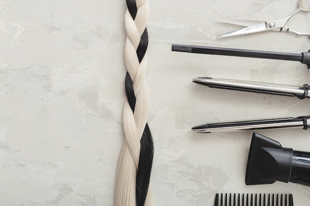 Outils de coiffeur et tresse de cheveux. Ciseaux, peignes, fer à cheveux sur fond gris