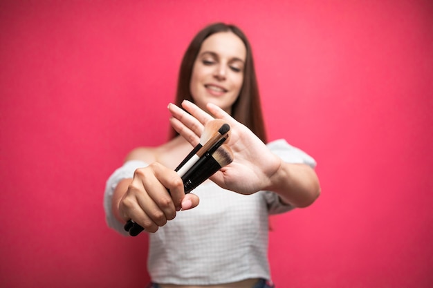 Outils cosmétiques professionnels. Jolie jeune femme tenant un pinceau de maquillage devant la caméra