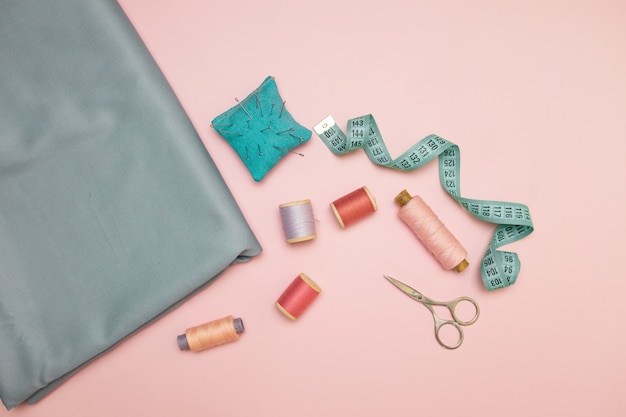 Outils de couture, point de couture tricoté pour la couture, ciseaux et bobines de fil de couleur sur fond rose avec fond pour le texte