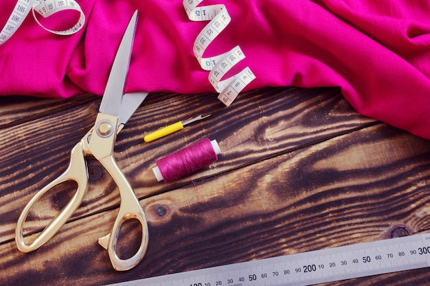 Outils de couture, tissu rose et fil sur un fond en bois