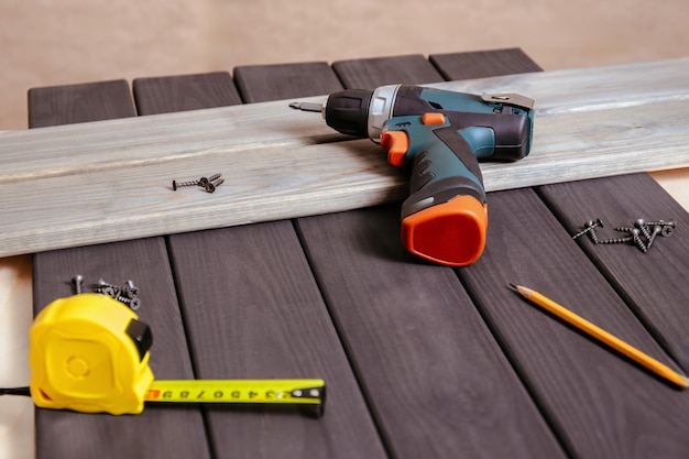 Outils et équipements de construction sur planches de bois, perceuse ou tournevis avec clous et règle de mesure, atelier de travail en bois avec outils