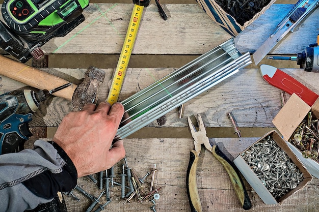 Outils Et Matériaux Pour L'installation Du Plafond Suspendu En Plaques De Plâtre. La Main Du Travailleur Prend Le Profil Pour L'installation. Mise à Plat Des Outils à Main. Réparation Simple Et Abordable De Locaux Avec Cloisons Sèches