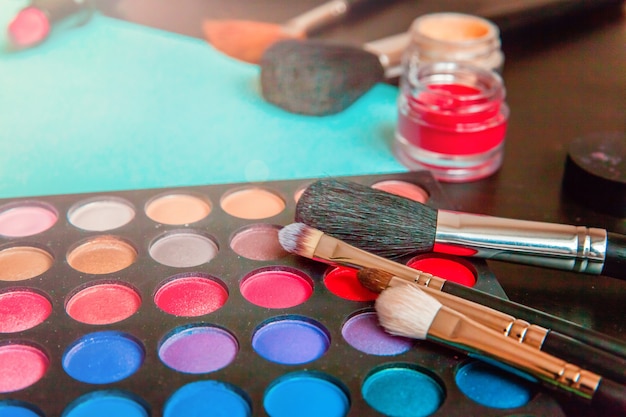 Outils pour le maquillage et les cosmétiques différentes nuances de palette de fard à paupières et pinceau de maquillage sur pastel bleu coloré à la mode