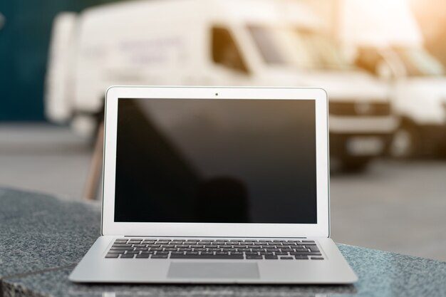 Ouvrez l'écran noir d'ordinateur portable avec l'immeuble de bureaux et le camion sur le concept de logistique de zone d'expédition de fond fournissant le service de transport de véhicule