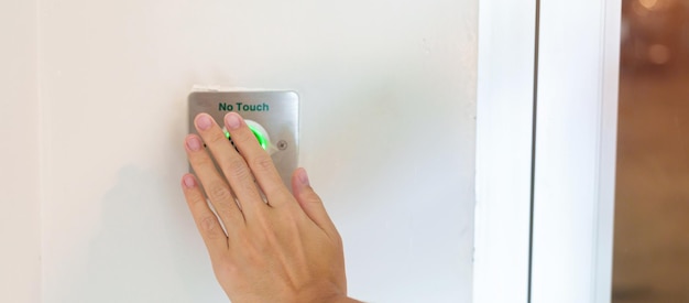 Ouvrez la porte à la main à l'aide d'un interrupteur sans capteur tactile sur le mur du bureau ou de l'appartement Technologie moderne sans contact et concept de sécurité