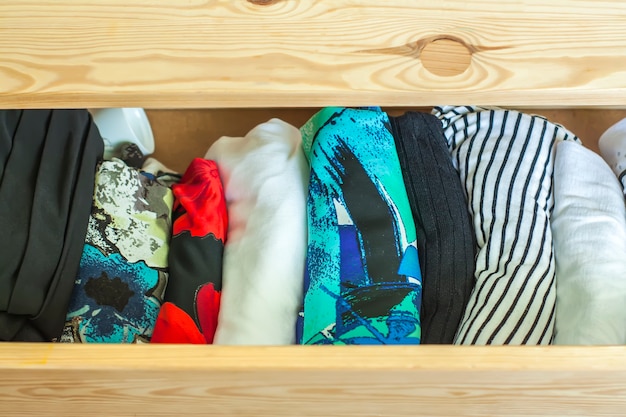 Ouvrez le tiroir de la commode en bois clair avec des vêtements colorés.
