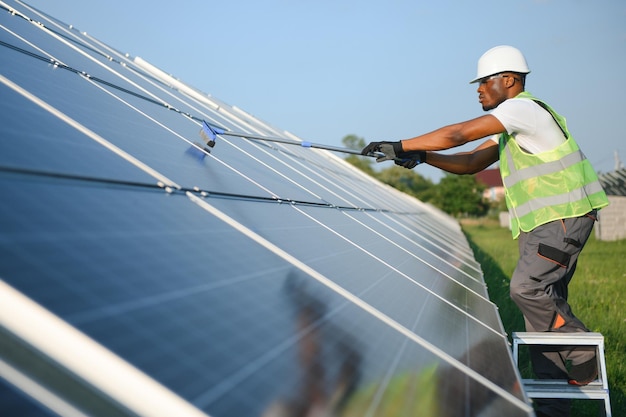 ouvrier afro-américain nettoyant un panneau solaire dans une centrale solaire