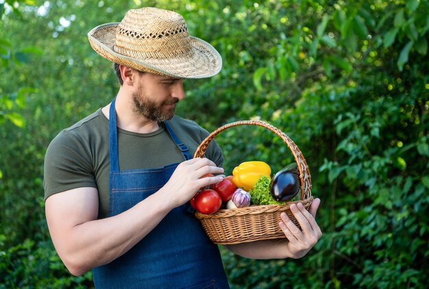 Ouvrier agricole en chapeau de paille tenir un panier plein de légumes