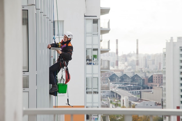 Un ouvrier d'alpinisme industriel est suspendu au-dessus d'un immeuble résidentiel tout en lavant le vitrage de la façade extérieure. L'ouvrier d'accès de corde se bloque sur le mur de la maison. Concept de travaux urbains. Espace de copie