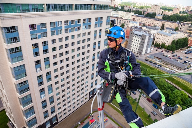 L'ouvrier d'alpinisme industriel s'accroche au-dessus du bâtiment résidentiel tout en installant