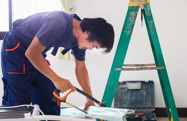 Ouvrier artisan sciant un tuyau Technicien installant une climatisation dans une maison de client Jeune réparateur fixant un climatiseur Concepts d'entretien et de réparation