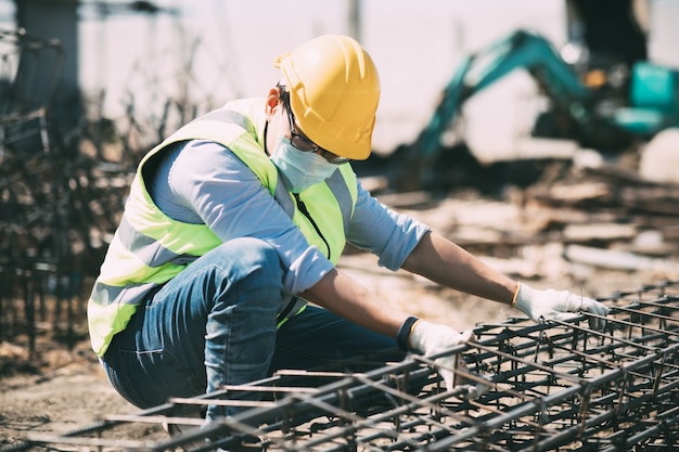 Ouvrier asiatique sur chantier. fabrication de barres de renfort en acier. porter un masque chirurgical lors d'une épidémie de coronavirus et de grippe